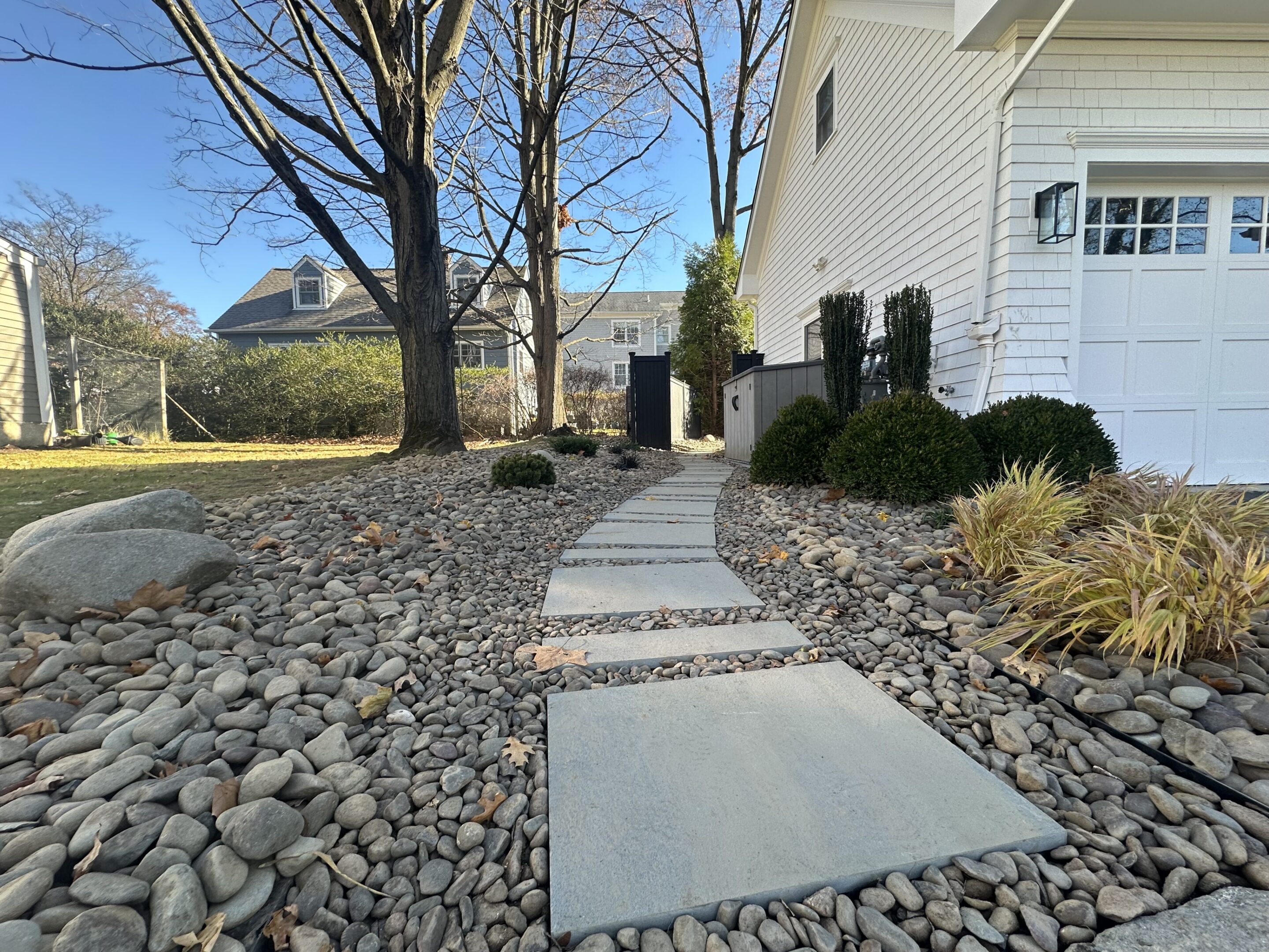 Modern stone pathway with large square slabs and surrounding rocks alongside a white house.
