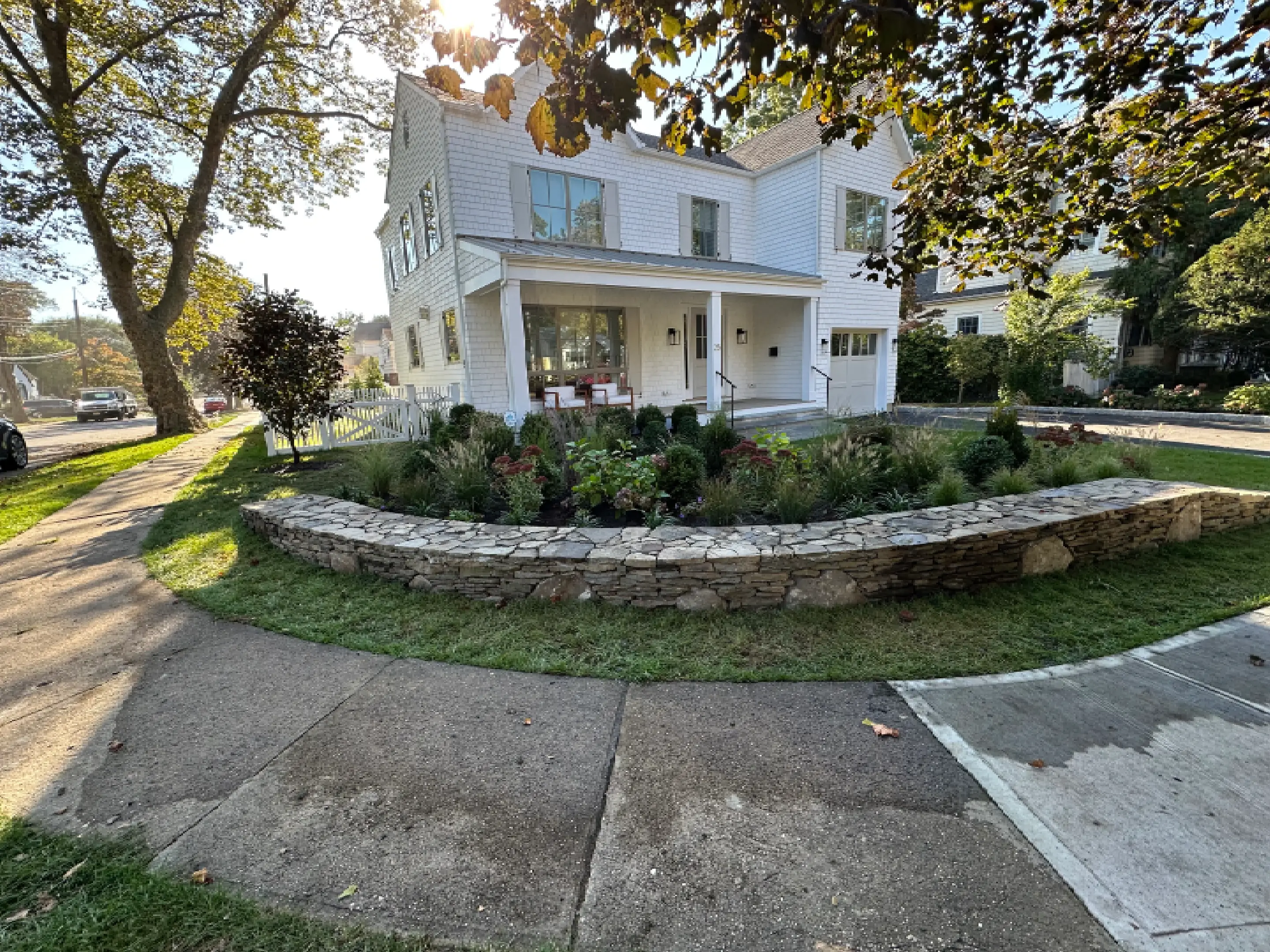 A white two-story house with a stone retaining wall and a garden in front.