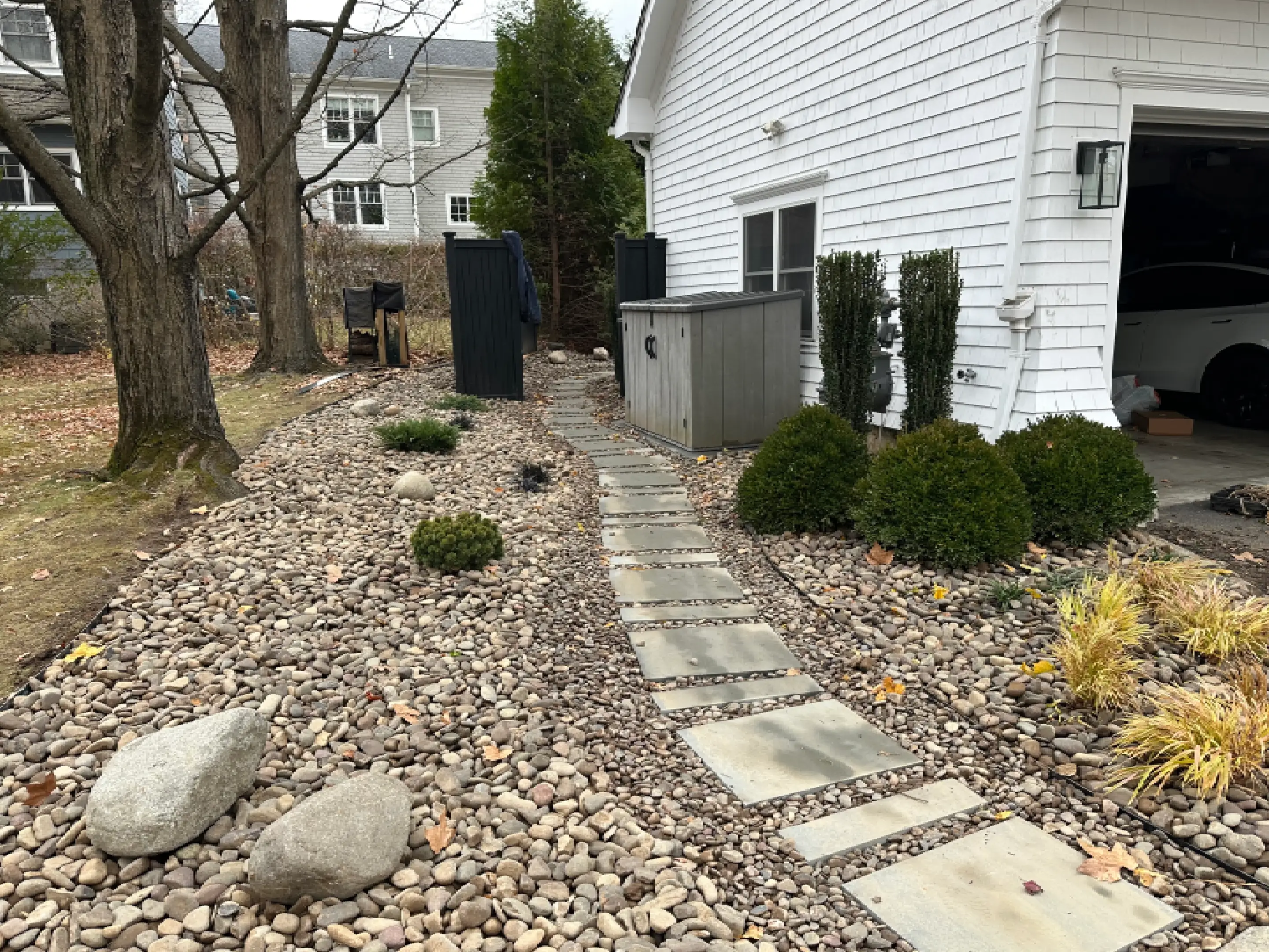 A stone pathway bordered by gravel leads along a white house's side yard.