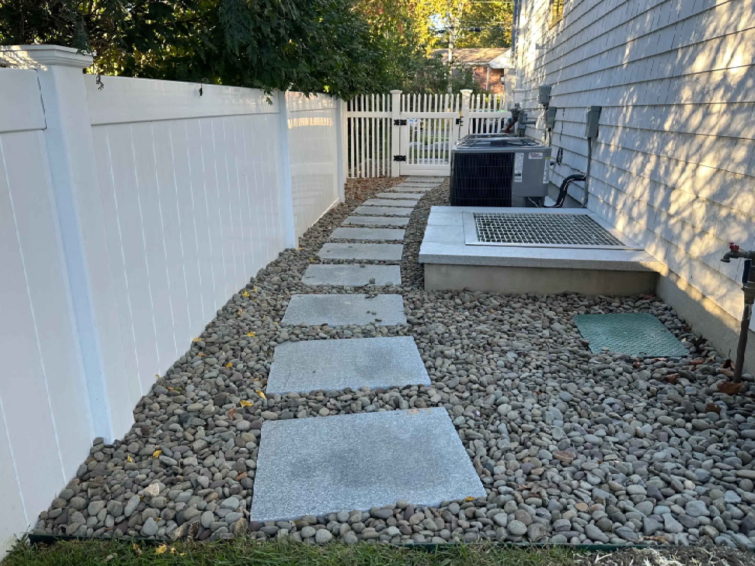 Stone pathway bordered by white fence and gravel beside a house.