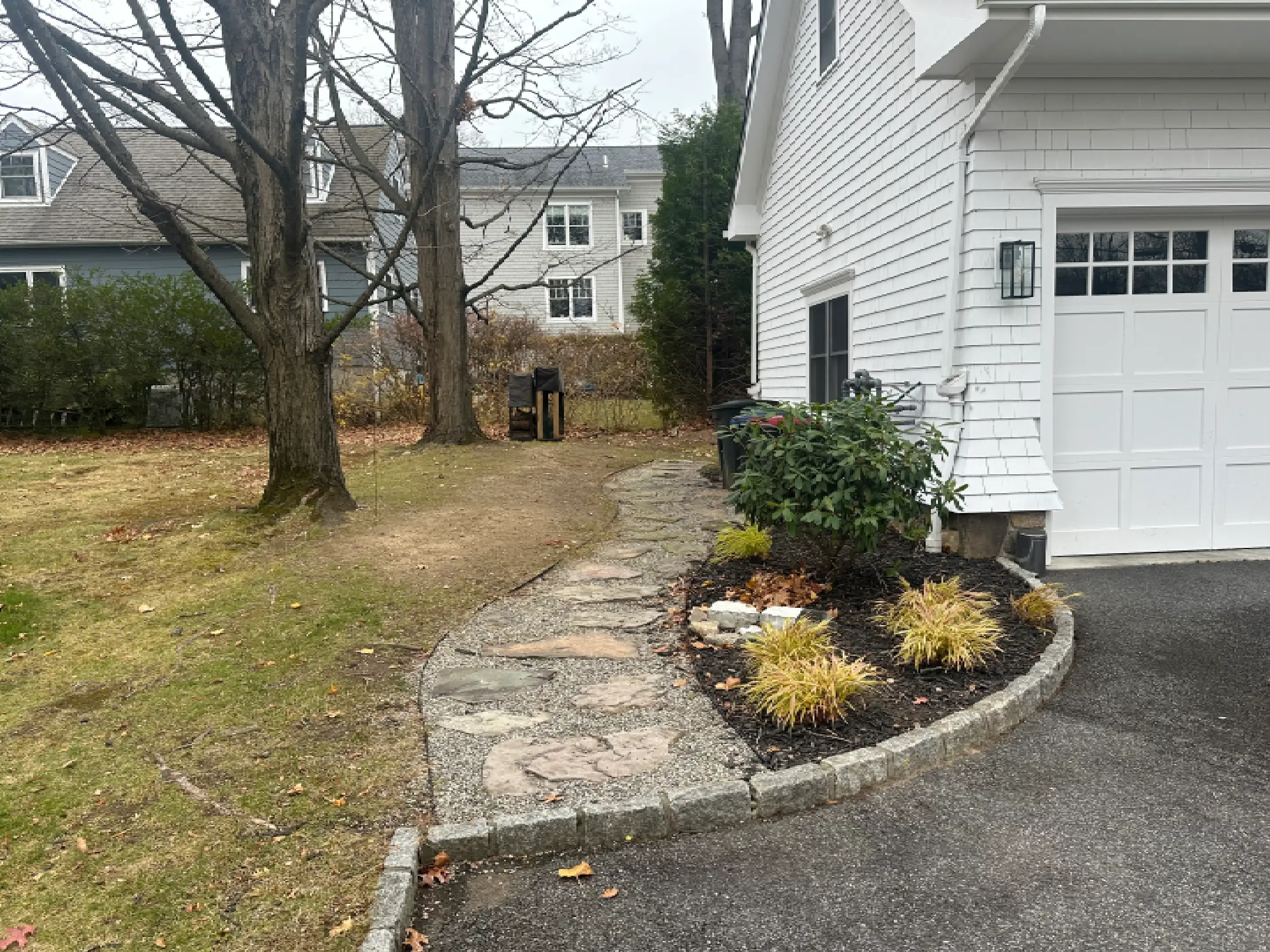 Curved stone pathway alongside a white house leading to a backyard.